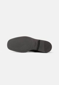 Melna kurpju zole ar gludu, plakanu dizainu, kurai ir teksturēts grip raksts un nemanāma zīmola identifikācija sānos.