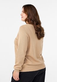 Maglione lavorato a maglia beige con un motivo testurizzato e polsini a costine, caratterizzato da un colletto rotondo e una vestibilità rilassata.