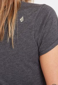 T-shirt gris à manches courtes en tissu doux, avec un petit logo doré sur l'épaule. Col arrondi et coupe ajustée.