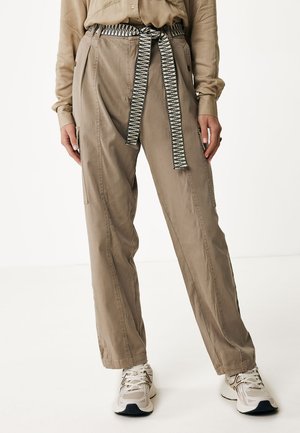 Beige broek met een hoge taille en zijzakken, met een dikke zwart-wit gestreepte stoffen riem, gecombineerd met lichte sportschoenen.