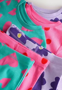 T-shirt di cotone colorate impilate, con toni di rosa e verde con motivi a cuori, viola con grandi fiori e lavanda uniforme, tutte con colli rotondi.