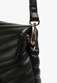 Borsa a tracolla nera trapuntata realizzata in pelle sintetica testurizzata, con chiusura dorata e tracolla rimovibile. Silhouette curva con dettagli cuciti.