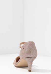Talons à bride de cheville en or rose avec une tige texturée, un bout pointu et un talon modeste. Présente une boucle décorative sur la bride.