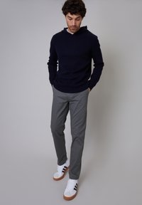 Dark navy hoodie, gray pants, and white sneakers with brown accents. Casual outfit with a relaxed fit and minimalistic design elements.