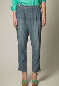 Pantaloni in denim blu chiaro a gamba affusolata con vita alta, tasche laterali e un leggero effetto sbiadito, abbinati a sandali verdi con cinturini.