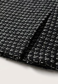 Tissu noir tissé affichant un motif texturé avec des accents blancs, présentant un design uniforme en grille et une finition douce.