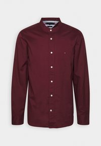 Camisa burdeos de botón con cuello mao, mangas largas, botones blancos y un pequeño logo bordado en el lado izquierdo del pecho. Tela de algodón.