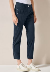 Pantalons cropped bleu marine en coton avec une taille élastique, dotés de poches latérales et d'accents de boutons en argent, portés avec des baskets blanches.