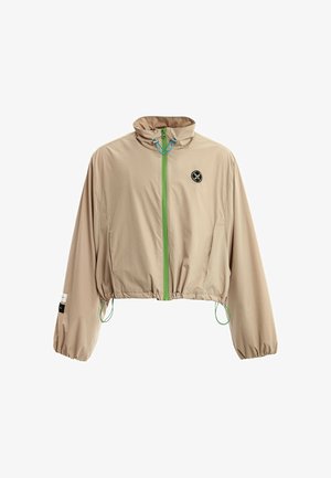 Chaqueta corta cortaviento de color marrón claro con puños elásticos, cremallera verde, cordones en el cuello y el dobladillo, y un pequeño logo redondo en el pecho.