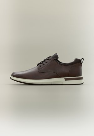 Chaussure décontractée marron en cuir à lacets avec semelle blanche et languette de tirage au talon, vue de profil sur un fond neutre.