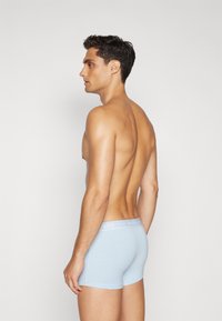 Helle blaue Baumwoll-Boxershorts mit weicher Textur. Verfügt über einen schlichten elastischen Bund mit dem weißen Logo "JACK & JONES". Modell von der Seite gezeigt.