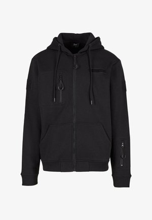 Mustapaita, jossa on avattava vetoketju, kiristettävä huppu, kaksi etutaskua, vetoketjullinen olkatasku ja tarranauha yksityiskohtia. Tasainen pinta, rento muotoilu.