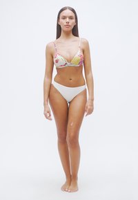 Μπικίνι τοπ με λουλουδάτο σχέδιο και λεπτές τιράντες, συνδυασμένο με απλές λευκές ψηλόμεσες βερμούδες, σχεδιασμένο για εφαρμοστή σιλουέτα.