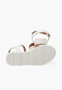 Sandalias blancas con detalles marrones, que cuentan con una suela de goma texturizada, correa de tobillo ajustable y un diseño de tacón cuadrado.