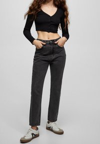 Svart kortärmad topp med knappar, matchad med högmidjade mörkgrå jeans och vita sneakers med beige och svarta detaljer.