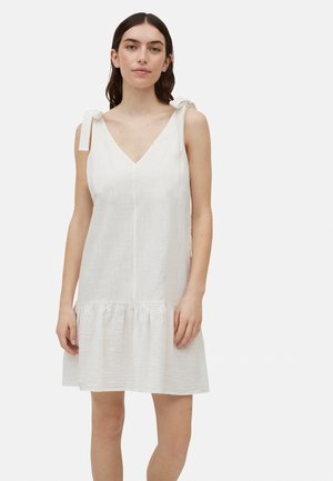 Vestido de lino blanco con escote en V, dos lazos en los hombros y un dobladillo con volantes en capas. La tela tiene un acabado texturizado sutil.