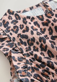 Tkanina se vzorem leopardí kůže s texturovaným povrchem, která má nařasené okraje a měkký růžový základ s černými a hnědými skvrnami.