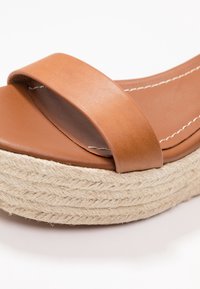 Bruna lädersandel med bred rem och plattform i naturligt snöre. Har sömnadsdetaljer och en slät yta på innersulan.