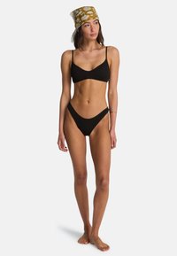 Bikini nero a coste con spalline sottili e slip a vita bassa. Un foulard marrone e bianco con motivo completa il costume da bagno.