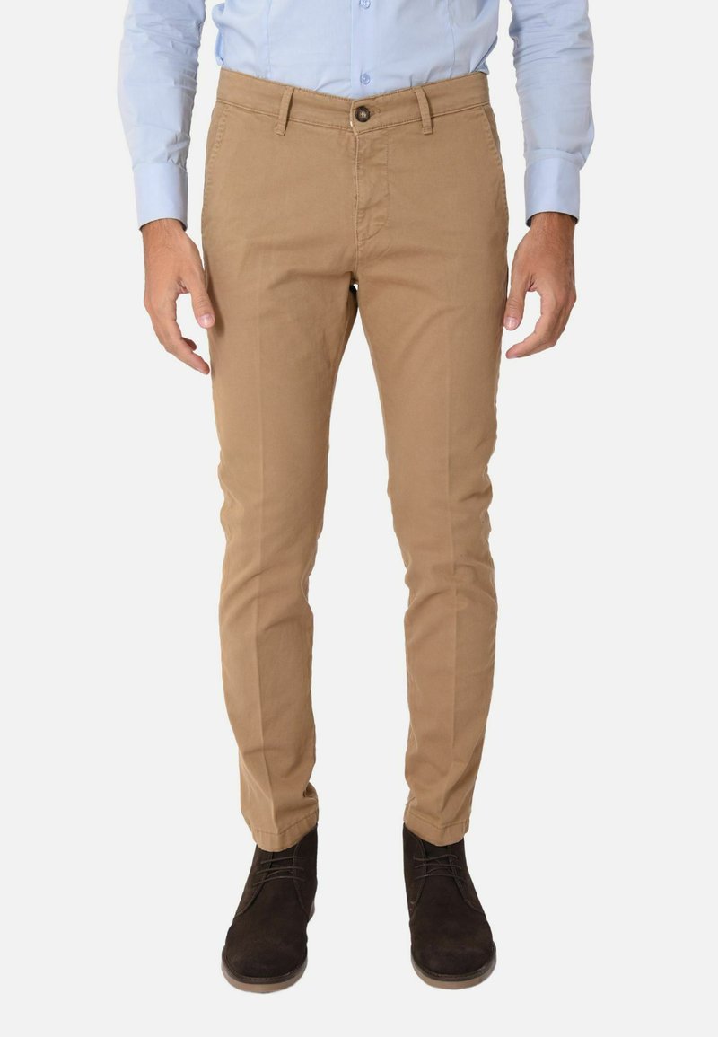 Chino in cotone color beige con vestibilità slim, dotato di chiusura con un solo bottone, passanti per cintura e tasche laterali. Indossati con scarpe marroni scure.