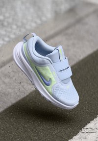 Hhellblauer Trainerschuh mit Obermaterial aus Mesh, grünen Akzenten, doppelten Klettverschlüssen und einem lila Nike-Swoosh an der Seite.