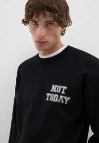 Felpa nera con scollo rotondo e testo ricamato bianco "NOT TODAY" sul petto. Tessuto morbido, vestibilità comoda, design minimale.