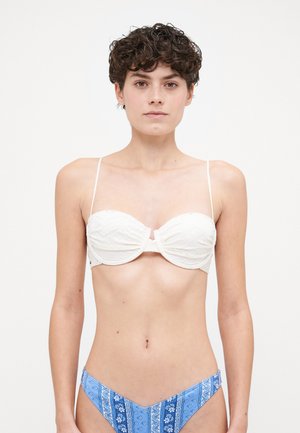 White strapless bikini top with textured fabric and zigzag pattern, paired with blue patterned bikini bottom featuring floral and stripe designs.