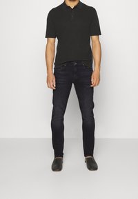 Musta poolsa socks ja lühikeste varrukatega särk, millele on lisatud tumedast sinisest slim-fit teksapükstest. Jalatsiteks on mustad nahast libisevad kingad.