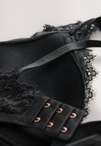 Nahaufnahme eines schwarzen Spitzen-BHs mit verstellbaren Trägern, auf denen "Lipsy" eingeprägt ist, und einem dreifachen Haken- und Ösenverschluss auf hellem Hintergrund.