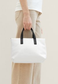 Sac tote blanc avec poignées noires, forme rectangulaire, surface texturée, logo en relief et fermeture éclair.
