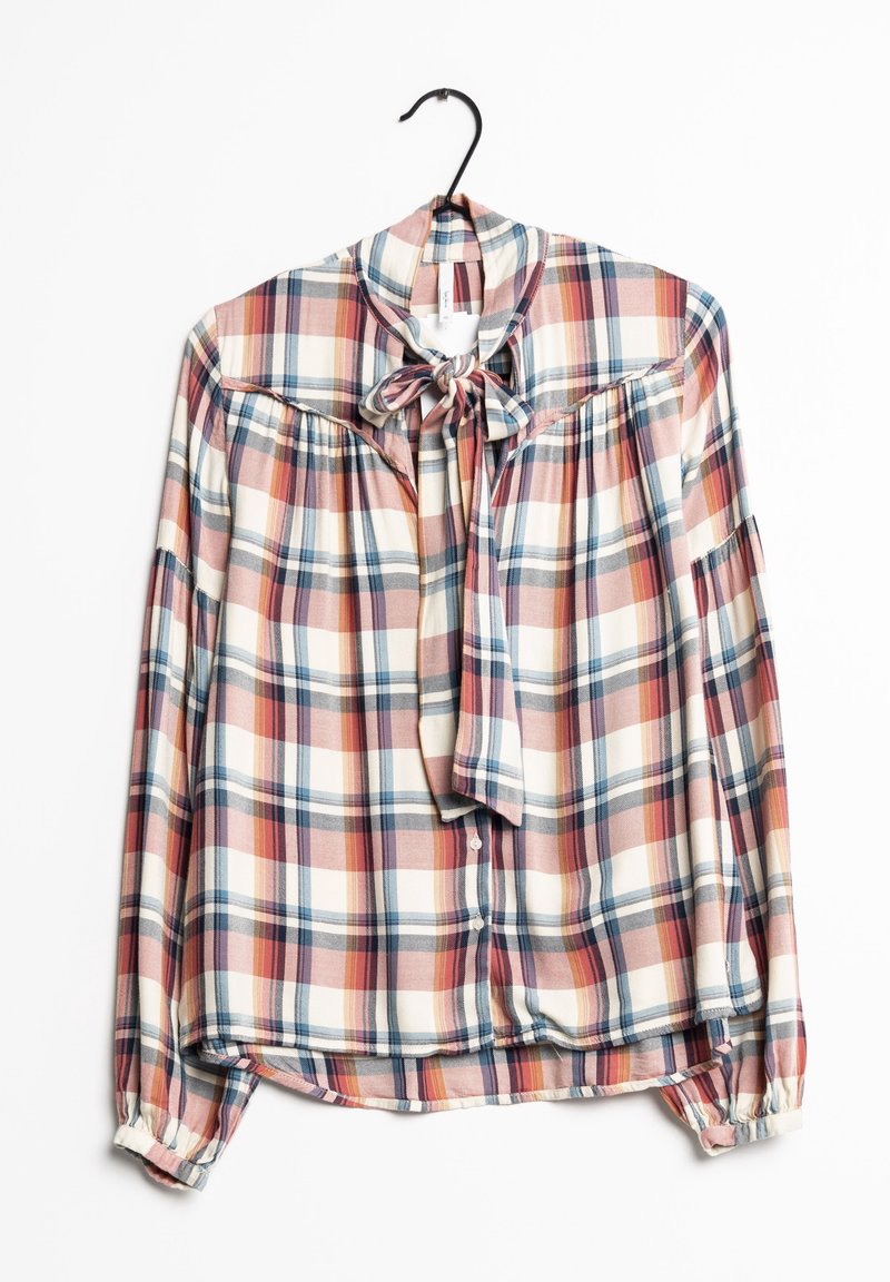 Blouse à manches longues à carreaux avec des rayures roses, blanches et bleues, col lavallière, boutonnière devant et poignets froncés sur un cintre noir.