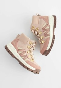 Paire de chaussures de randonnée roses et beiges avec des semelles épaisses marron et des œillets métalliques dorés, exposée sur un fond clair.