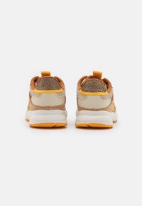 Beige och orange sportskor med texturerade accenter, som har en vadderad krage, dragflik och en tjock vit sula med orange mönster.
