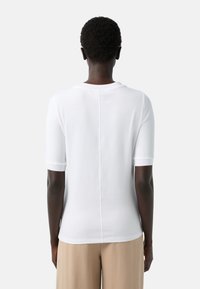 Hvid kortærmet t-shirt lavet af glat bomuld med rund hals og lige kant, der har en syet søm i midten af ryggen.