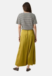 Haut à manches courtes rayé avec des lignes noires et blanches, associé à une jupe maxi verte olive. La jupe a une taille élastique et une texture lisse.
