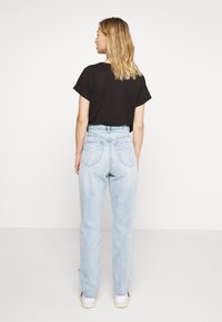 Jeans de tom azul claro com uma cintura alta, apresentando um padrão de costura em forma de coração nos bolsos traseiros, combinados com uma blusa preta texturizada de manga curta.