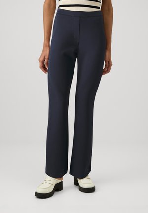 Pantalons marins avec une taille ajustée et une jambe évasée. Tissu lisse sans motifs visibles. Associés à des chaussures ivoire avec une semelle épaisse.