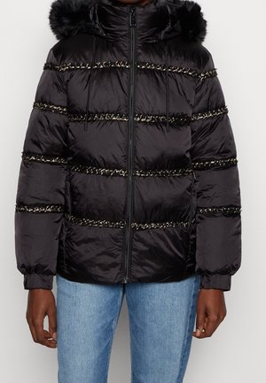 Chaqueta negra acolchada con bandas horizontales acolchadas y ribete texturizado, cremallera frontal, capucha forrada de piel, usada con jeans azul claro.