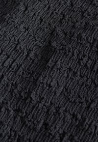 Tissu tricoté noir avec un motif texturé et en relief créant une surface complexe et tactile sur l'ensemble du matériau.