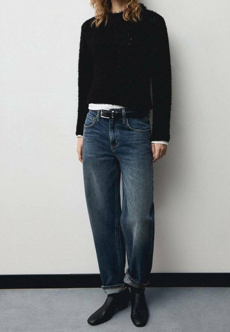 Pull noir en tissu duveteux associé à un jean en denim à lavage clair et coupe ample, agrémenté d'une ceinture noire. Porté avec des bottines noires.