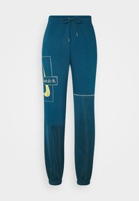 Pantalones de chándal en verde azulado, fabricados con un tejido suave, que presentan un estampado gráfico con el texto "just do it" y el logo de Nike, puños elásticos y una cinturilla con cordón ajustable.