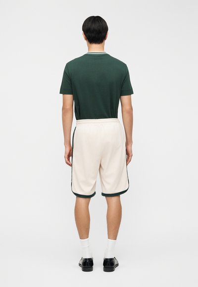 Πράσινο πουκάμισο με κοντά μανίκια και στρογγυλή λαιμόκοψη, συνδυασμένο με μπεζ σορτς που έχουν σκοτεινές πράσινες λεπτομέρειες και ελαστική μέση.
