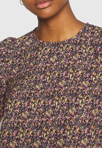 Gros plan d'une femme portant un haut en fleurs multicolores avec des manches courtes bouffantes et un col rond.