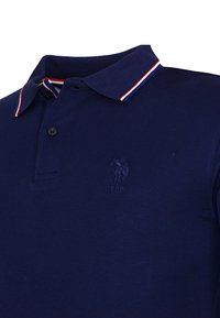 Námornícky modré polo tričko s dvoma gombíkmi, golierom s prúžkami v červeno-bielo-modrej farbe a vyrazeným logom USPA polového hráča na hrudi.