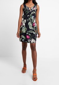 Blommig klänning med marinblå bakgrund, ärmlös design, elastisk midja, nyckelhålskänning och matchad med orange remsandaler.