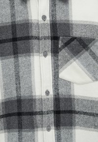 Koszula w kratę w białym i szarym kolorze, wykonana z miękkiego flanelu. Posiada guziki, kieszonkę na piersi oraz wyraźny wzór w kratę w różnych odcieniach.