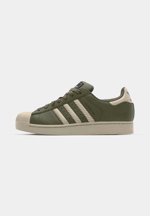 Sneakers verde in pelle con punta in tela beige, tre strisce beige sui lati e pannello posteriore testurizzato. Suola in gomma.