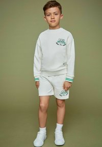 Witte sweatshirt en shorts set met groene accenten en geborduurd logo. Soepele stof, relaxte pasvorm en ontwerp met ronde hals en geribde manchetten.