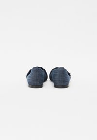 Denim slip-on sko i mørkeblå med frynset kant, flate såler og en teksturert overflate, med et enkelt, minimalistisk design.
