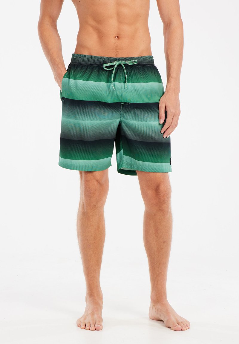 Costumi da bagno a righe verdi e nere con cintura elastica e cordino. Il tessuto ha una superficie liscia e presenta due tasche laterali.